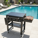 A BBQ Boards® 30" Blackstone Griddle Side Cutting Board stands on a tiled patio next to a pool, with lounge chairs, plants, and a privacy fence—perfect for stylish flat top prep by BBQ Boards®.