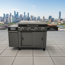 A BBQ Boards® 36" Blackstone Griddle Side Cutting Board is attached to a black outdoor grill with four knobs and a side burner on a rooftop patio, city skyline in the background under a clear blue sky.