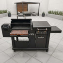 A BBQ Boards® Blackstone Pellet Grill Combo with front or side cutting board, grill prep station, two side tables, and control panel sits on a spacious patio with minimalist furniture and potted plants in the background.