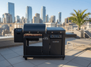 A BBQ Boards® Blackstone Pellet Grill Combo Front or Side Cutting Board by BBQ Boards® is set on a rooftop patio with lounge chairs and a palm plant, overlooking the city skyline and tall buildings in the background.