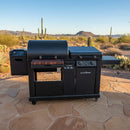 A BBQ Boards® Blackstone Pellet Grill Combo Front or Side Cutting Board by BBQ Boards® is showcased on a stone patio in a desert landscape, surrounded by cacti, shrubs, and distant mountains beneath a clear blue sky.