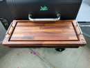 The BBQ Boards® GMG Daniel Boone/Ledge Pair, Front & Side Cutting Boards (Pair) are displayed on a grill, highlighting their wood grain and juice groove, with the classic Green Mountain Grills handle and control panel in view.