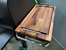 A BBQ Boards® GMG Daniel Boone/Ledge Trio Front, Side & Pellet Bin Cutting Boards set of three with metal handles and juice grooves sits on a BBQ prep station, hooks below. Light-colored wall and floor are visible in the background.
