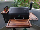 The BBQ Boards® GMG Daniel Boone/Ledge Trio Cutting Boards (set of 3) by BBQ Boards® make grilling prep easy, fitting perfectly on your pellet grill near a white patio railing and lush green plants.