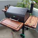 A black GMG Daniel Boone Ledge Trio grill with BBQ Boards® front, side, and pellet bin cutting boards (set of three) by BBQ Boards® on the patio creates a handy BBQ prep area with spices, plants, and a gray fence in the background.