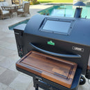 A sleek black Green Mountain Grills Ledge pellet grill with BBQ Boards® GMG Ledge Prime 2.0 Front & Side Cutting Boards (Pair), set on a tiled patio beside a swimming pool and outdoor seating area.