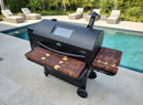 A GMG Peak Prime 2.0 grill poolside on a tiled patio features BBQ Boards® Front & Side Cutting Boards, with lounge chairs, greenery, and Green Mountain Grills accessories in the background.