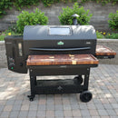 The BBQ Boards® GMG Peak Prime 2.0 Pair, Front & Side Cutting Boards (Pair) by BBQ Boards® are set up on a spacious grill workspace outdoors, perfectly complementing the patio grilling area surrounded by greenery and stone.
