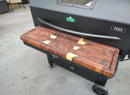 The BBQ Boards® GMG Peak Prime 2.0 Front Cutting Board is mounted to the black grill, providing extra prep space and an elegant look for Green Mountain Grills accessories on a concrete surface.