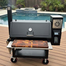 A BBQ Boards® Lone Star Grillz 20" x 42" Front Cutting Board is on a large black smoker grill with a digital control panel, set on a patio deck by the pool, with palm plants and a hot tub in the background.