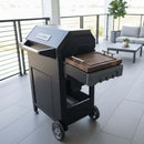 A BBQ Boards® Masterbuilt AutoIgnite Series 545 Side Cutting Board is paired with a black grill on a modern patio with sofa, coffee table, and potted plant—ideal for seamless grilling and prep.