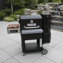 A BBQ Boards® Masterbuilt Gravity Series 800 Side Cutting Board by BBQ Boards® is featured on a black grill with a wood side shelf, set on a tiled patio with a scenic garden and stone waterfall in the background.