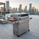 A BBQ Boards® Monument Grills Denali 610 Side Cutting Board is displayed on a sleek rooftop terrace with a city skyline and infinity pool at sunset.