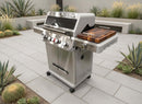 A BBQ Boards® Monument Grills Mesa 405BZ Side Cutting Board is featured on a four-burner stainless steel gas grill, set on a tiled patio surrounded by succulents and cacti in a modern outdoor space.
