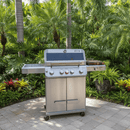 A BBQ Boards® Monument Grills Mesa 405BZ Side Cutting Board is shown on a stone patio, surrounded by lush green palm trees and tropical plants in a garden setting.