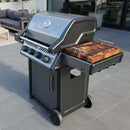 The BBQ Boards® Napoleon Freestyle Side Cutting Board by BBQ Boards® offers convenient grill-side prep on your gray tiled patio, pairing perfectly with a modern gas grill featuring four control knobs and a built-in thermometer.