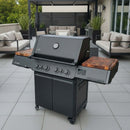 A modern black gas grill with BBQ Boards® Napoleon Prestige 500 Connected Side Cutting Boards (Matching Pair) stands on a tiled patio, surrounded by cushioned outdoor sofas and tall potted plants in a stylish backyard.