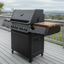 A large black Napoleon Prestige 500 gas grill with closed lid, multiple knobs, and wooden side shelves sits on a deck—featuring BBQ Boards® Connected Side Cutting Boards (matching pair) for easy prep and serving.