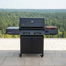 A BBQ Boards® Napoleon Prestige 500 Connected Side Cutting Board by BBQ Boards® sits on a black outdoor gas grill with four knobs and a side burner, positioned on a tiled patio overlooking a forest under a cloudy sky.