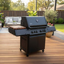 A sleek black gas grill with four burners stands on a patio, featuring the BBQ Boards® Napoleon Prestige 500 Connected Side Cutting Board by BBQ Boards®, surrounded by outdoor furniture and backyard greenery.