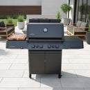 A black outdoor gas grill with a built-in thermometer and side shelves featuring the BBQ Boards® Napoleon Prestige 500 Connected Side Cutting Board stands on a tiled patio, alongside modern patio furniture and potted plants.