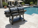 A BBQ Boards® Pit Boss Pellet Gas Combo Side Cutting Board by BBQ Boards® is shown on a large black Pit Boss Pellet Gas Combo grill, set on a tiled patio near a swimming pool with lounge chairs and patio furniture in the background.