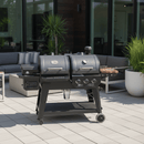 The BBQ Boards® Pit Boss Pellet Gas Combo Side Cutting Board by BBQ Boards® is a modern black outdoor grill with multiple burners and a smoker, set on a patio in front of a contemporary house with large windows, patio furniture, and potted plants.
