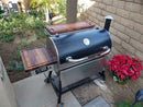 The BBQ Boards® Recteq RT-700 Pair, Front & Side Cutting Boards by BBQ Boards® create an ideal patio cooking station, set alongside a brick wall near a garden bed and a bright red poinsettia.
