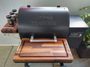 A Traeger Ironwood 650 grill on a patio features BBQ Boards® Traeger Ironwood 650 Front & Side Cutting Boards (Pair) creating a neat BBQ space, with seasoning containers on the side shelf and digital controls visible.