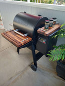 The BBQ Boards® Traeger Ironwood 650 Front & Side Cutting Boards (Pair) by BBQ Boards® creates an ideal BBQ prep space on your patio, fitting perfectly on your smoker grill next to a potted plant.