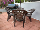 Four brown plastic chairs surround a round outdoor table on a red-tiled patio. In the background, a BBQ Boards® Traeger Ironwood 885 Front & Side Cutting Boards (Pair) sit by the grill, with purple bushes near a light gray fence.