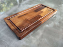 The BBQ Boards® Traeger Ironwood Front Cutting Board features a deep groove, various wood tones, and a stamped logo in the top right corner—ideal as a BBQ prep station on any gray textured surface.