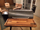 A BBQ Boards® Traeger Pro 34 Front Cutting Board is on a Traeger grill with a closed lid, placed on a patio near a glass table with cushioned chairs and a door leading inside.