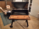A BBQ Boards® Traeger Pro 34 Front Cutting Board sits on a black pellet grill with its lid open, showcasing an empty grate. This BBQ Boards® accessory is the perfect fit for your patio grilling setup.