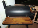 A pair of BBQ Boards® Traeger Pro 780 Front & Pellet Bin Cutting Boards sit on a Traeger grill’s wooden deck, providing extra prep space beside the embossed logo lid and spice containers.