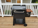 A black Weber Searwood 600 pellet grill with a digital control panel and wooden side shelf sits on a deck, paired with the BBQ Boards® Weber Searwood 600 Pellet Bin Cutting Board, in front of a white porch railing.