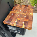 A BBQ Boards® Weber Searwood XL 600 Pellet Bin Cutting Board is mounted to a Weber Searwood XL 600 grill above its digital temperature panel, with grass and concrete visible in the background.