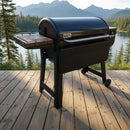 A BBQ Boards® Weber Smoque & XL Side Cutting Board by BBQ Boards® is set on a black outdoor grill atop a wooden deck, with scenic views of a lake, pine trees, and mountains in the daylight.