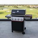 A BBQ Boards® Weber Spirit Reinvented Side Cutting Board is attached to a black and silver gas grill with three knobs, set on a tiled patio overlooking a golf course and lush green landscape.