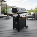 A modern outdoor deck features patio furniture and green plants, with a black gas grill topped by the BBQ Boards® Weber Spirit Reinvented Side Cutting Board from BBQ Boards®, which sits beside four control knobs.