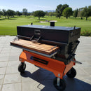 A Yoder Smokers grill with a BBQ Boards® Yoder Flat Top Front Cutting Board sits on a patio overlooking a green golf course and trees beneath a clear blue sky.