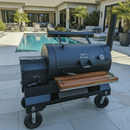 A BBQ Boards® Yoder YS1500 Front Cutting Board sits on a poolside grill station on a modern patio, with lounge chairs, palm trees, and a sparkling swimming pool enhancing the luxurious outdoor setting.