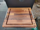 The BBQ Boards® Yoder YS480 or YS640 Side Cutting Board features a wood prep surface with metal handles, a juice groove around the edge, and the BBQ Chiefs logo engraved on the bottom right corner.