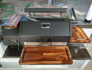 The BBQ Boards® Yoder YS640 Trio Front, Side & Pellet Bin Cutting Boards (Set of 3) by BBQ Boards® provide spacious prep surfaces on your grill, perfect for upgrading your outdoor cooking setup. Grass and dirt are visible in the background.