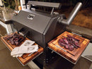 The BBQ Boards® Yoder YS640 Trio Set adds three cutting boards—front, side, and pellet bin—for optimal meat prep on your Yoder smoker grill. White grill gloves on the left tray highlight this ideal outdoor nighttime workspace upgrade.