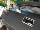 A BBQ Boards® Yoder YS640 Trio Cutting Boards Set is shown on the grill’s front, side, and pellet bin, offering the ultimate workspace upgrade. On the side shelf are Stone beer, Rib Rack BBQ sauce, bourbon, and greenery in the background.