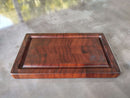 The BBQ Boards® Basic BBQ Board® 16" x 9" reversible cutting board, featuring a grooved edge, dark wood grain, and engraved logo, rests on a gray reflective surface.