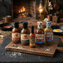 Five bottles from Bear & Burton's Ultimate Sauce Bundle sit on a wooden board in a rustic kitchen, with coarse salt, pepper, a skillet, and a fried egg nearby—showcasing the versatility of Bear & Burton's sauces.