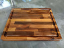 The Beastliest BBQ Board® 21" x 17" Cutting Board by BBQ Boards®, with varied wood tones, a grooved edge, and the “BBQ Board” logo in one corner, rests on a gray countertop.