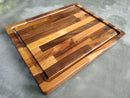 The Beastliest BBQ Board® 21" x 17" Cutting Board by BBQ Boards® features a striped wood pattern and a groove along the edge, shown on a gray surface.